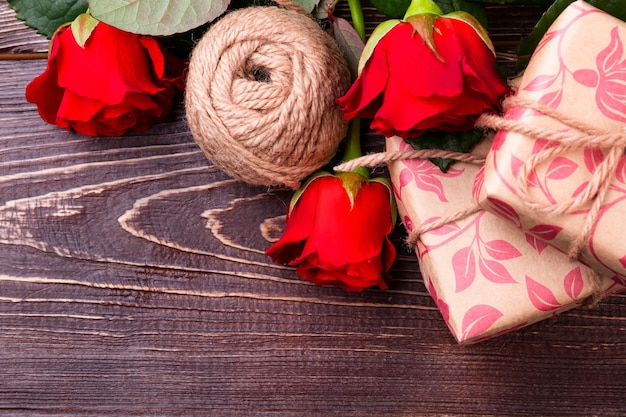 Rote Rosen und Geschenkbox. Blumen in der Nähe von Garnballen. Kunst, Geschenke zu machen. Schönheit des Handwerks.