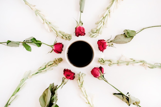 Rote Rosen und weiße Blumen rahmen mit Kaffeetasse auf weißer Oberfläche ein