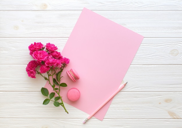 Rote Rosenstiftmakronen und leere rosa Papierkarte auf hölzernem Hintergrund
