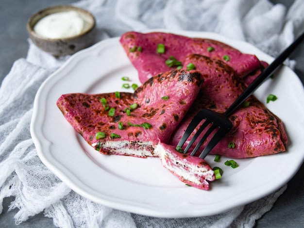 Rote Rote-Bete-Wurzeln Pfannkuchen, rosa dünne Rübenkrepps füllten mit Sahne Käse und Frühlingszwiebeln auf grauem Hintergrund