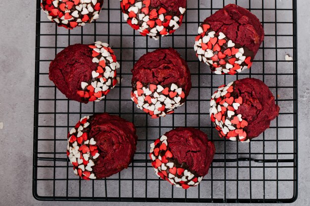 Rote runde Kekse, verziert mit herzförmigem Pulver zum Valentinstag, auf einem schwarzen Metallgitter, grauer Steinhintergrund