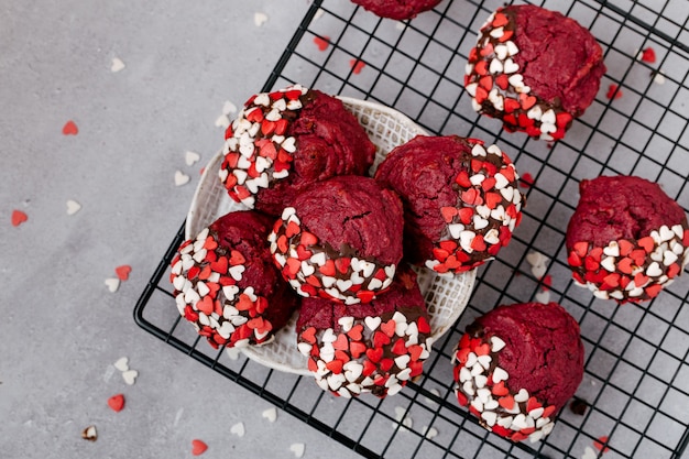 Rote runde Kekse, verziert mit herzförmigem Pulver zum Valentinstag, auf einem schwarzen Metallgitter, grauer Steinhintergrund