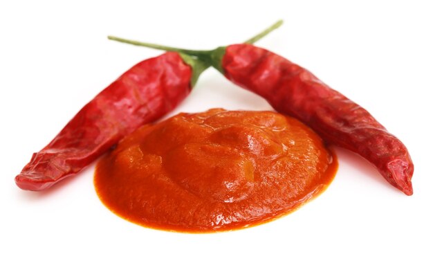 Rote scharfe Chilis mit Paste auf weißem Hintergrund