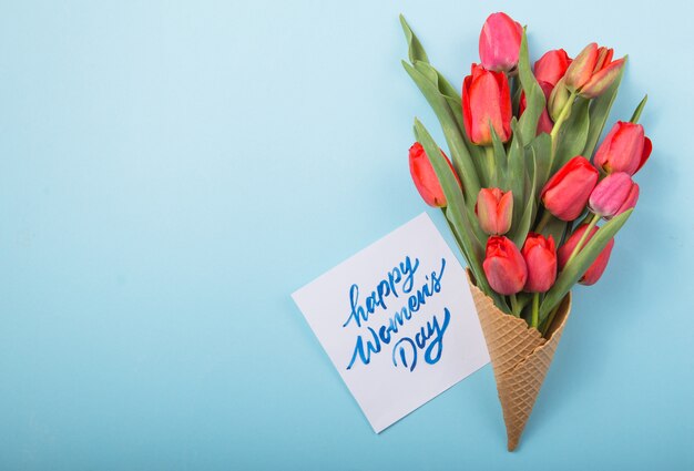 Rote schöne Tulpen in einer Eiscreme-Waffeltüte mit Frauentag der Karte auf einem konkreten Hintergrund. Konzeptionelle Idee eines Blumengeschenks. Frühlingsstimmung