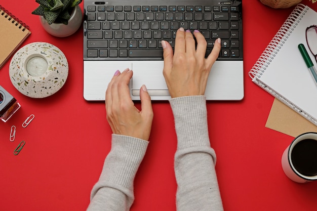 Rote Schreibtisch- und Frauenhände des modernen Arbeitsplatzes der Ebenenlage auf Tastatur des Laptops