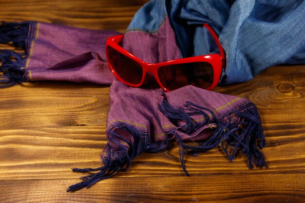 Rote Sonnenbrille und Sommerschal auf hölzernem Hintergrund. Modeaccessoires für Damen. Sommerurlaub und Reisekonzept