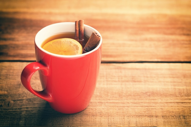 Rote Tasse heißen Tees mit Zitrone und Zimt auf einem Holztisch.