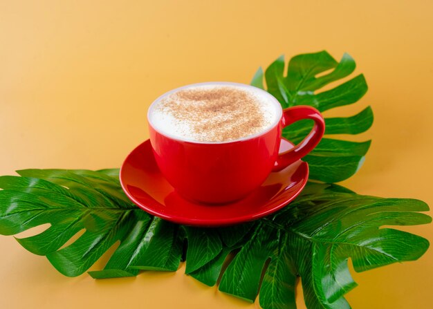 Rote Tasse Kaffee auf großen grünen Blättern auf gelbem Hintergrund