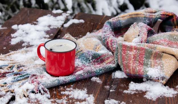 Rote Tasse Kaffee und Schal auf Holztisch im Schneesturm