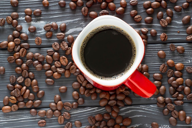 Rote Tasse Kaffee zwischen Bohnen auf einem Holztisch