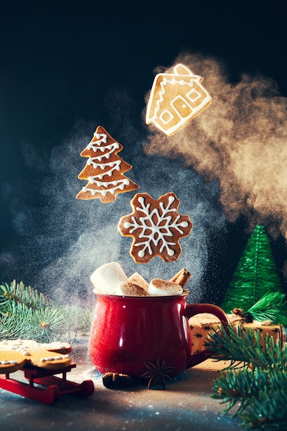 Rote Tasse mit Marshmallows und Zimt und fliegenden Weihnachtslebkuchenplätzchen