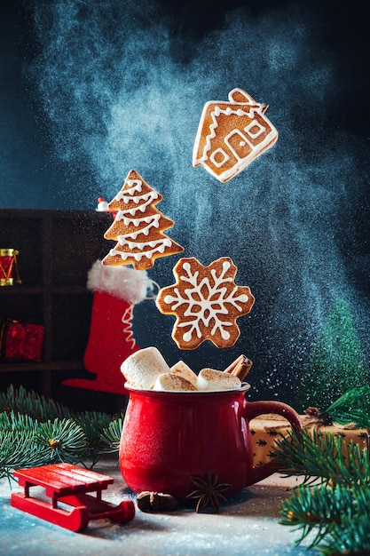 Rote Tasse mit Marshmallows und Zimt und fliegenden Weihnachtslebkuchenplätzchen