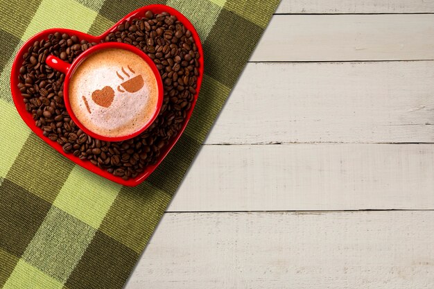 Rote Tasse und Kaffee Untertasse in Herzform mit dekoriertem Kaffee auf altem Holzhintergrund. Draufsicht. Geschrieben ich liebe Kaffeeform in Kaffee in Englisch.