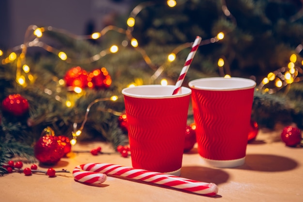 Rote Tasse vor dem Hintergrund des Weihnachtsbaumes, leuchtende Girlanden und rote Kugeln