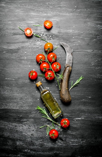 Rote Tomaten mit Rosmarin und einer Flasche Olivenöl. Auf schwarzem rustikalem Hintergrund.