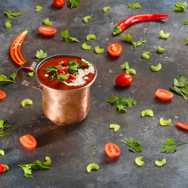 Rote tomatensuppe in der kupfernen schale auf dunkelheit.