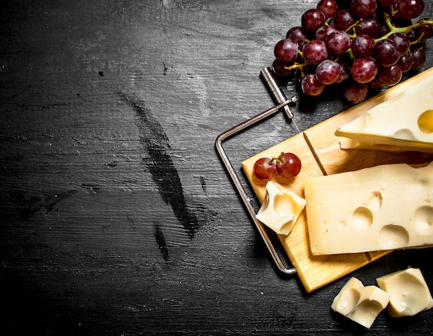 Rote Trauben und Käsestücke auf schwarzem Holztisch.