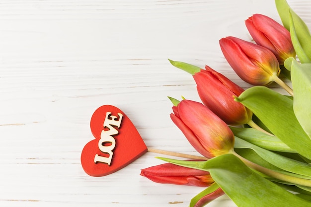 Rote Tulpen auf weißem Holzhintergrund mit einem roten Holzherz mit der Aufschrift Liebe Feiern zum Geburtstag oder zur Hochzeit des Internationalen Frauentags