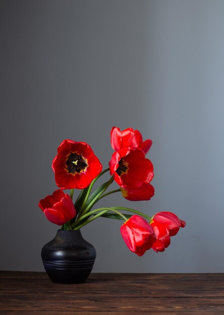 Rote Tulpen in dunkler Keramikvase auf Holztisch