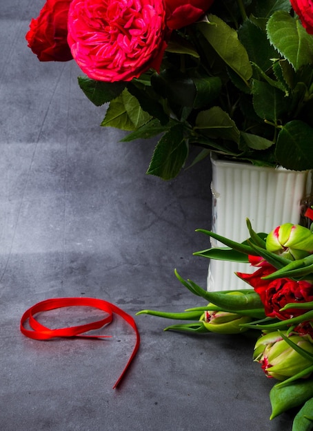Rote Tulpen und Rosen mit rotem Band isoliert auf konkretem Hintergrund Tag des Sieges oder Tag des Vaterlandverteidigers 9. Mai Symbol