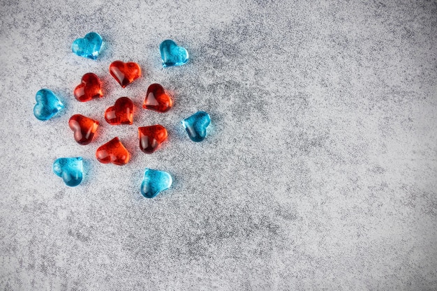 Rote und blaue dekorative durchscheinende Herzen, die in Kreisen auf grauer Oberfläche angeordnet sind