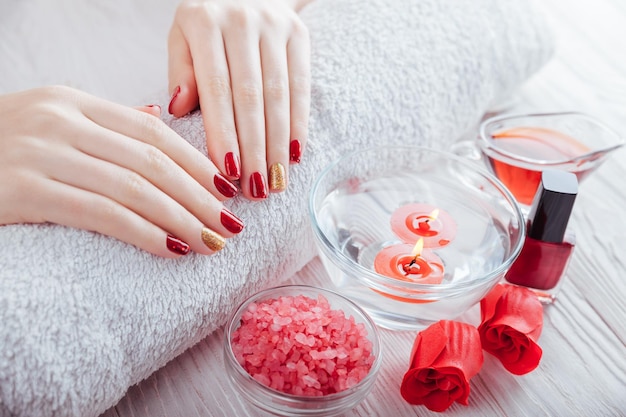 Rote und goldene Maniküre mit Spa-Essentials auf weißem Holztisch