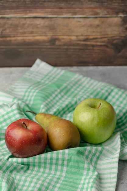 Rote und grüne äpfel mit frischer birne auf grüner tischdecke.