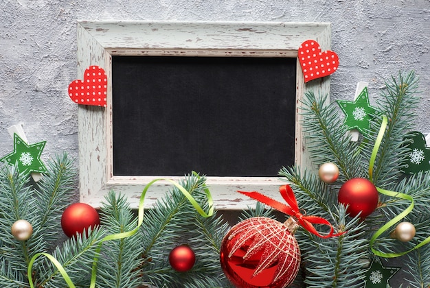 Rote und grüne Weihnachtsdeko: Tannenzweige, Beeren und Christbaumkugeln auf grauem Beton,