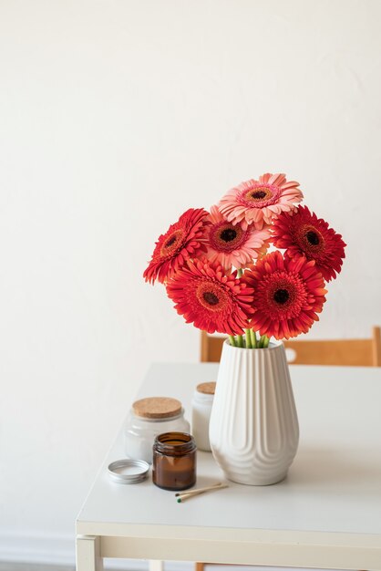 Rote und rosa Gerbera-Gänseblümchen in weißer Vase auf Küchentisch und weißem Wandhintergrund