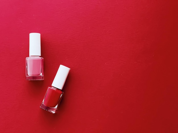 Rote und rosafarbene Nagellackflaschen auf rotem Hintergrund Maniküre und Schönheitskosmetikkonzept