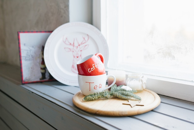 Rote und weiße Becher für Tee und Kaffee auf einem Fensterbrett in einer Wohngestaltung