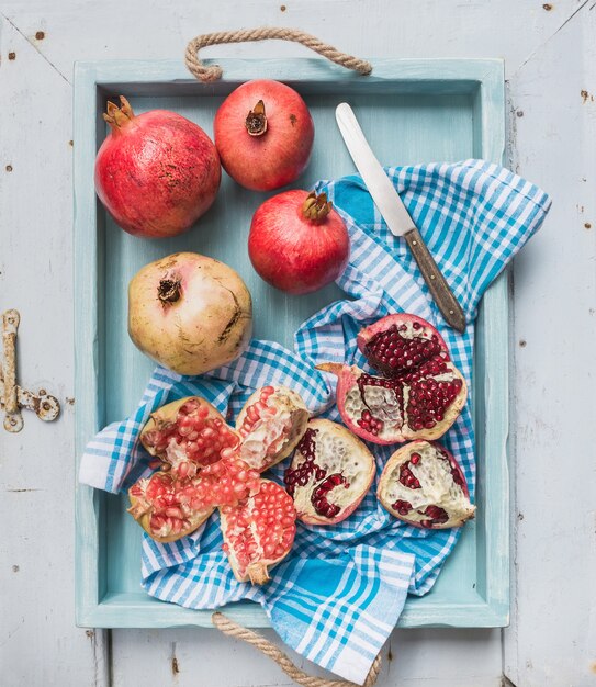 Rote und weiße Granatäpfel mit Messer auf Geschirrtuch im blauen Behälter über Licht gemaltem Holztisch