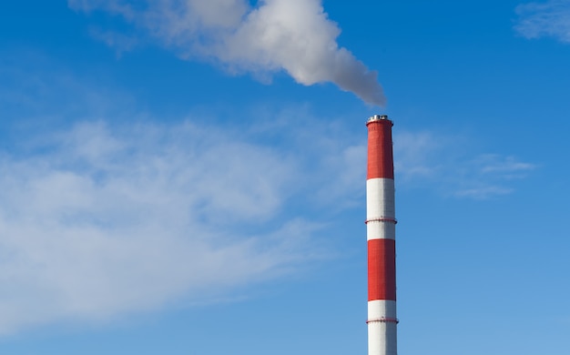 Rote und weiße rauchende Schornsteine der Fabrik auf blauem Himmel.