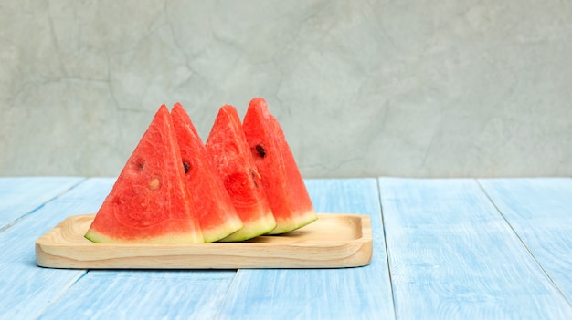 Rote Wassermelone auf einer Platte und einem blauen Holztisch.