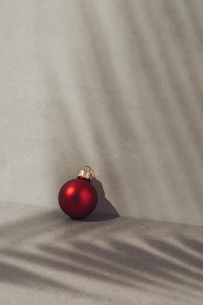 Rote Weihnachtskugel auf konkretem Hintergrund Palmblattschatten Minimales Begrüßungskonzept für das neue Jahr