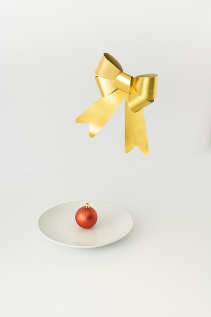 Rote Weihnachtskugeldekoration auf weißer Platte mit goldener Schleife, die oben schwebt