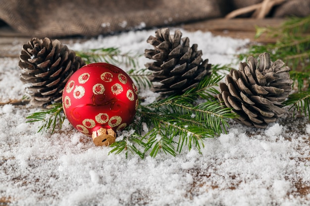 Rote Weihnachtskugeln mit Tannenzweigen und Tannenzapfen auf Schneetisch, Nahaufnahme, Platz für Text, horizontal