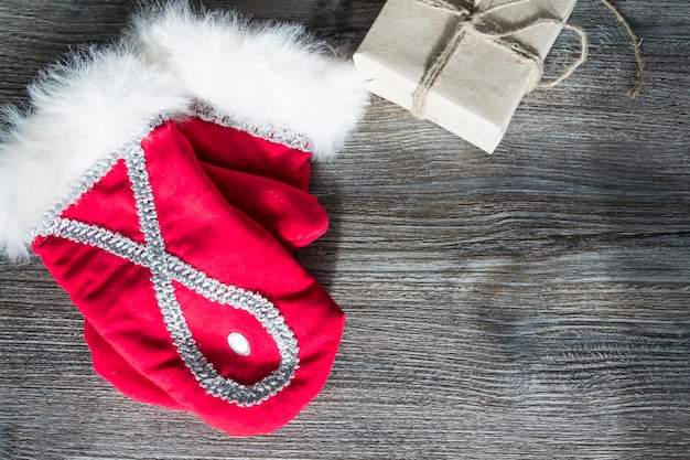 Rote Weihnachtsmann-Fäustlinge und eine Schachtel mit Geschenken in handwerklicher Verpackung auf einer Holzoberfläche