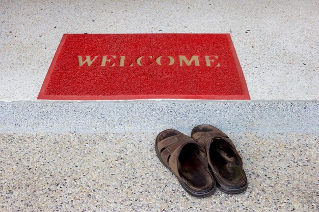 rote Willkommensmatte auf der Treppe und alte Sandalen