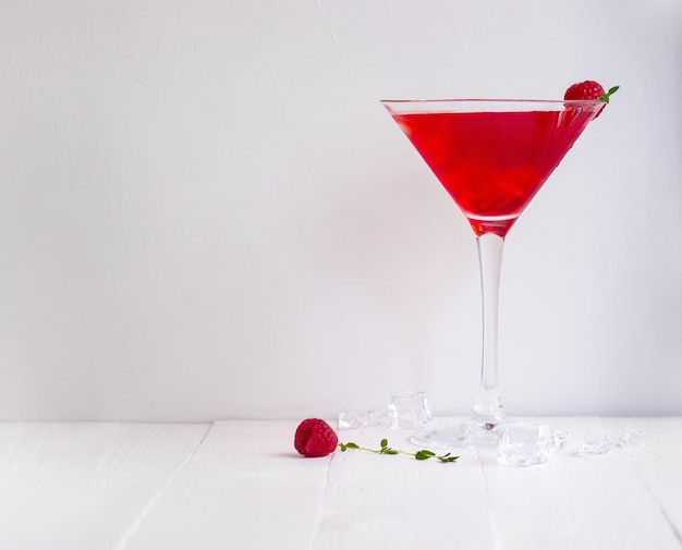 Roter Alkoholcocktail mit Himbeeren und Thymian auf dem weißen Holztisch