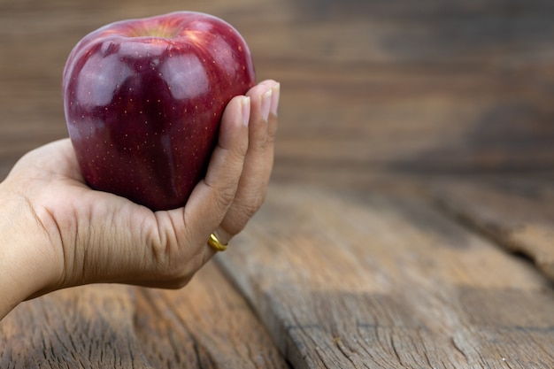 Foto roter apfel in der hand mit einem hölzernen hintergrund.