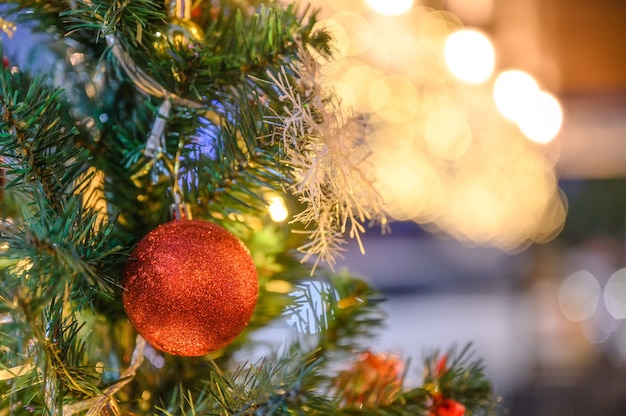 Roter Ball hängt an Tannenbaum mit verschwommenem Licht zur Weihnachtszeit