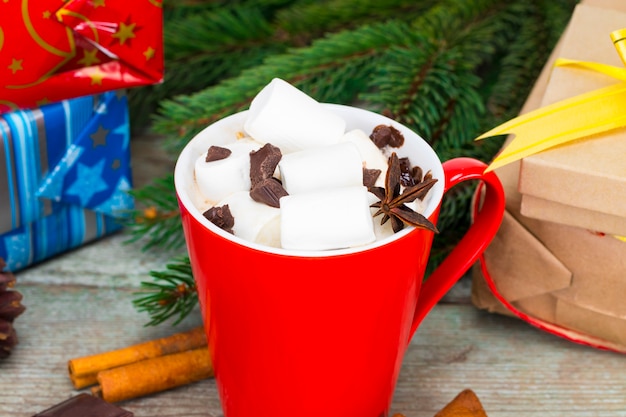 Roter becher mit heißer schokolade mit geschmolzenem marshmallow auf hölzernem hintergrund mit geschenken und weihnachtsdekorationen