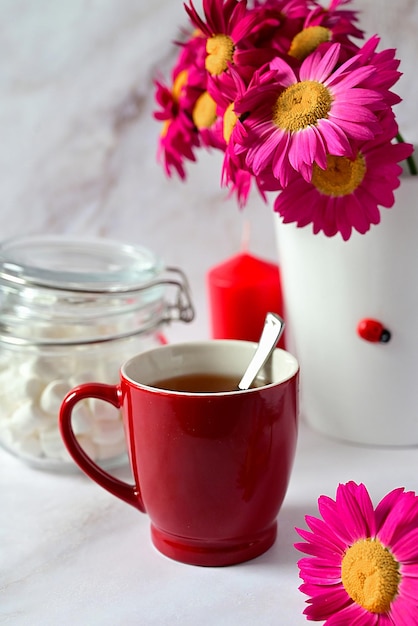 Roter Becher mit Tee auf dem Hintergrund eines Blumenstraußes aus roten Blumen