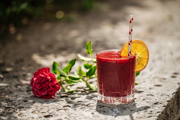 Roter Beeren-Smoothie in einem Glas mit einem Strohhalm auf einem Stein mit Blume