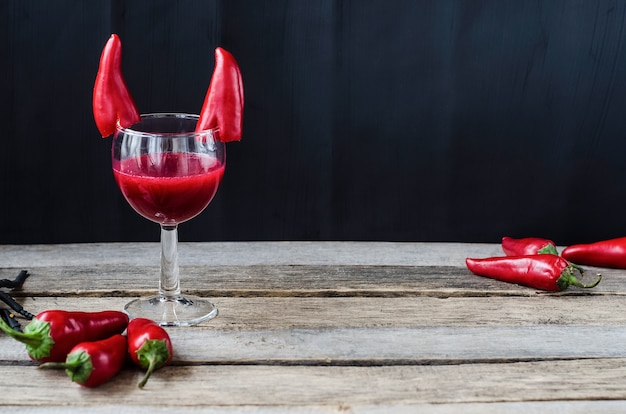 Roter Cocktail für Halloween-Feier mit Teufelshörnern Chilischoten verziert. Auf Holzoberfläche