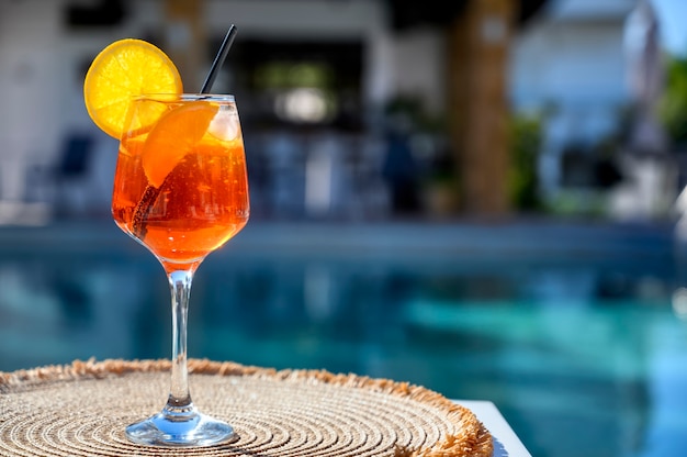 Roter Cocktail mit Orangenscheibe und Eis nahe einem Hotelpool