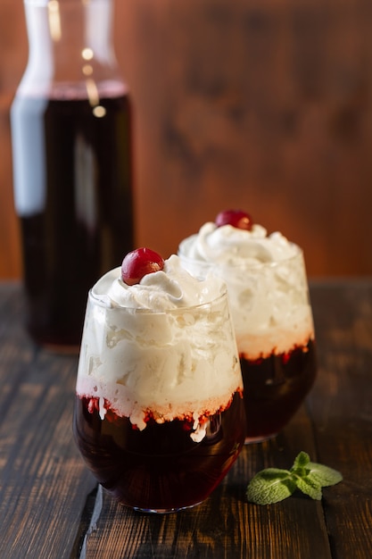 Roter Cocktail mit Schlagsahne-Topping im Glas auf brauner Holzoberfläche