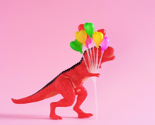 Roter Dinosaurier hält farbenfrohe Ballons auf rosa Hintergrund