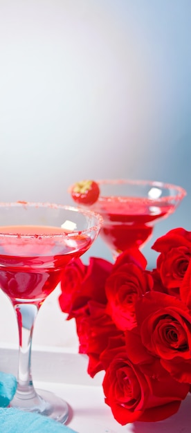 Roter exotischer alkoholischer Cocktail in klaren Gläsern und in roten Rosen auf dem weißen Holztablett für romantisches Abendessen.